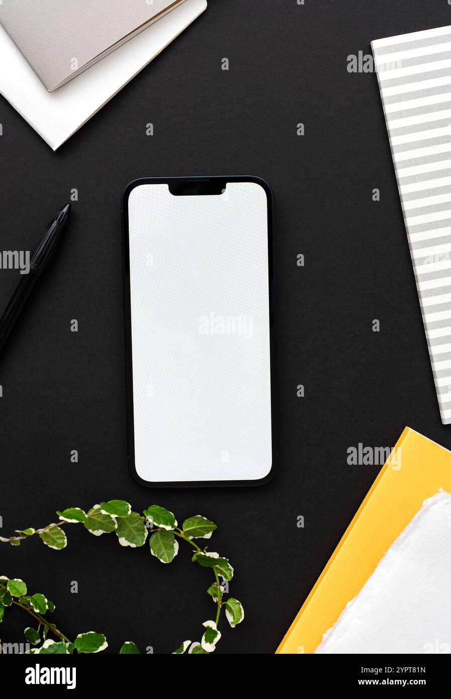 Smartphone moderno su un tavolo nero con decorazioni verdi in stile casa, blocchi appunti gialli e grigi - elegante configurazione dello spazio di lavoro. Vista dall'alto. Copia spazio Foto Stock