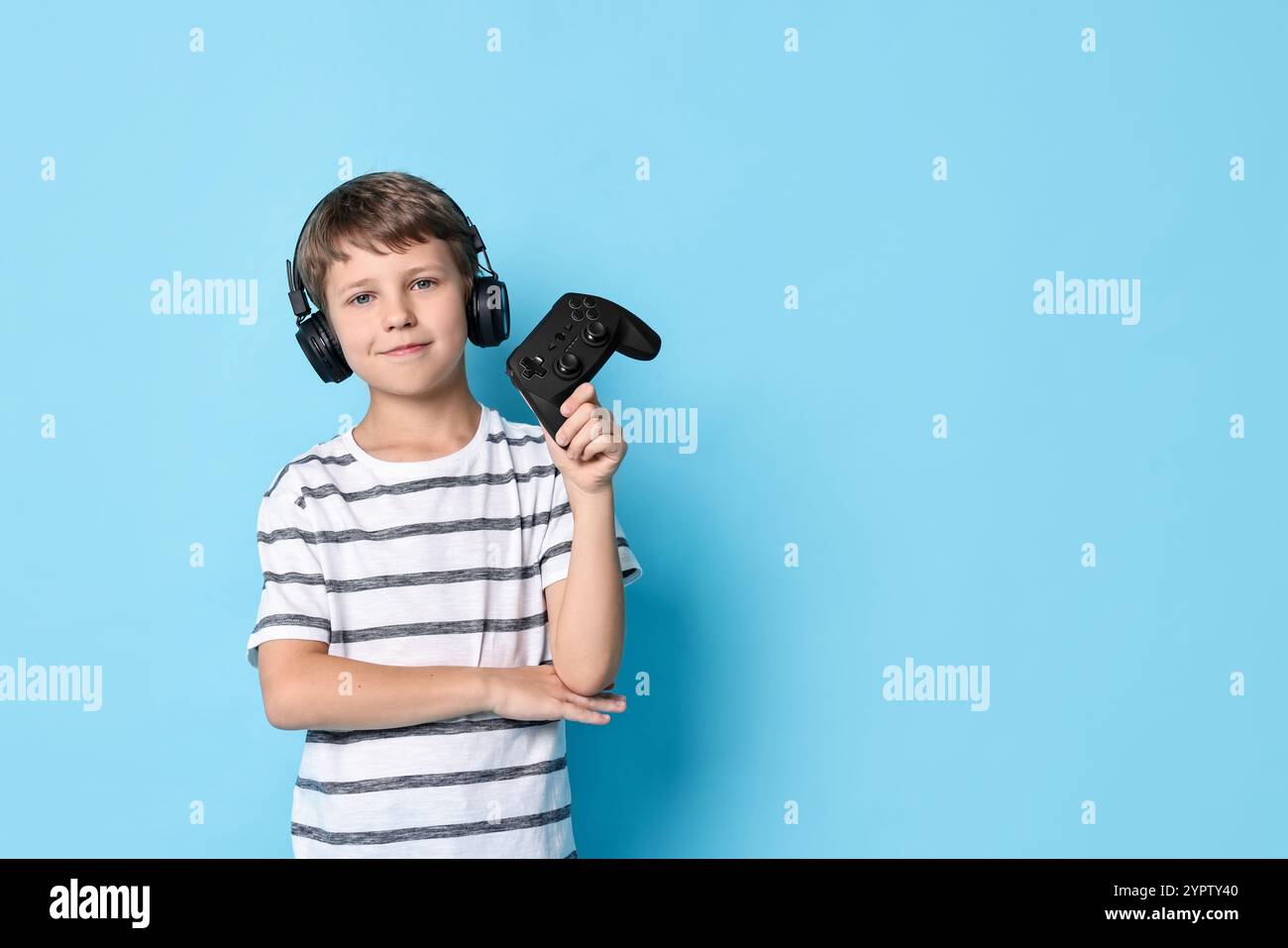 Simpatico bambino in cuffie con controller su sfondo azzurro. Spazio per il testo Foto Stock