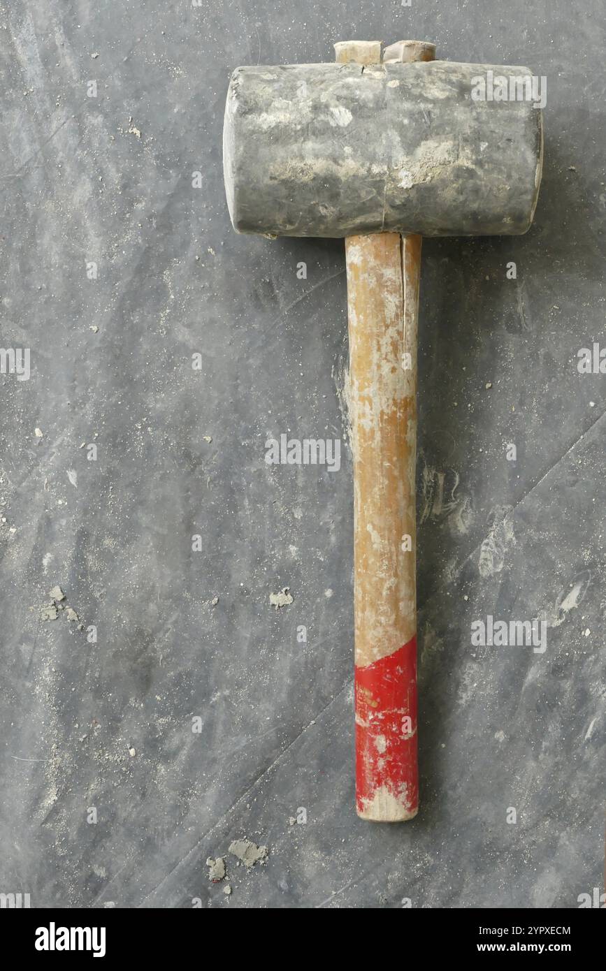 Martello in gomma con cemento spruzza su foglio di plastica scuro con contrassegno rosso sull'impugnatura Foto Stock