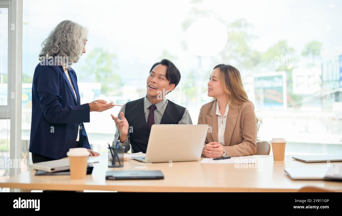 Un uomo d'affari asiatico professionista e intelligente in una tuta formale condivide con fiducia le sue idee e spiega un progetto al suo team durante una collaborazione Foto Stock