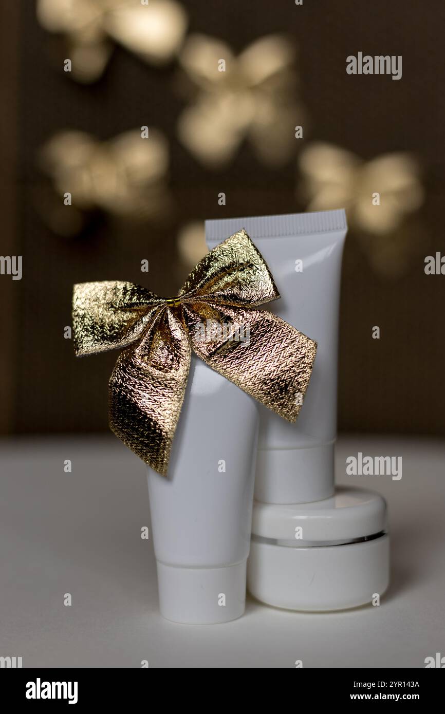 Un'immagine splendidamente composta di vasetti e tubetti cosmetici bianchi accentuati da un fiocco dorato Foto Stock