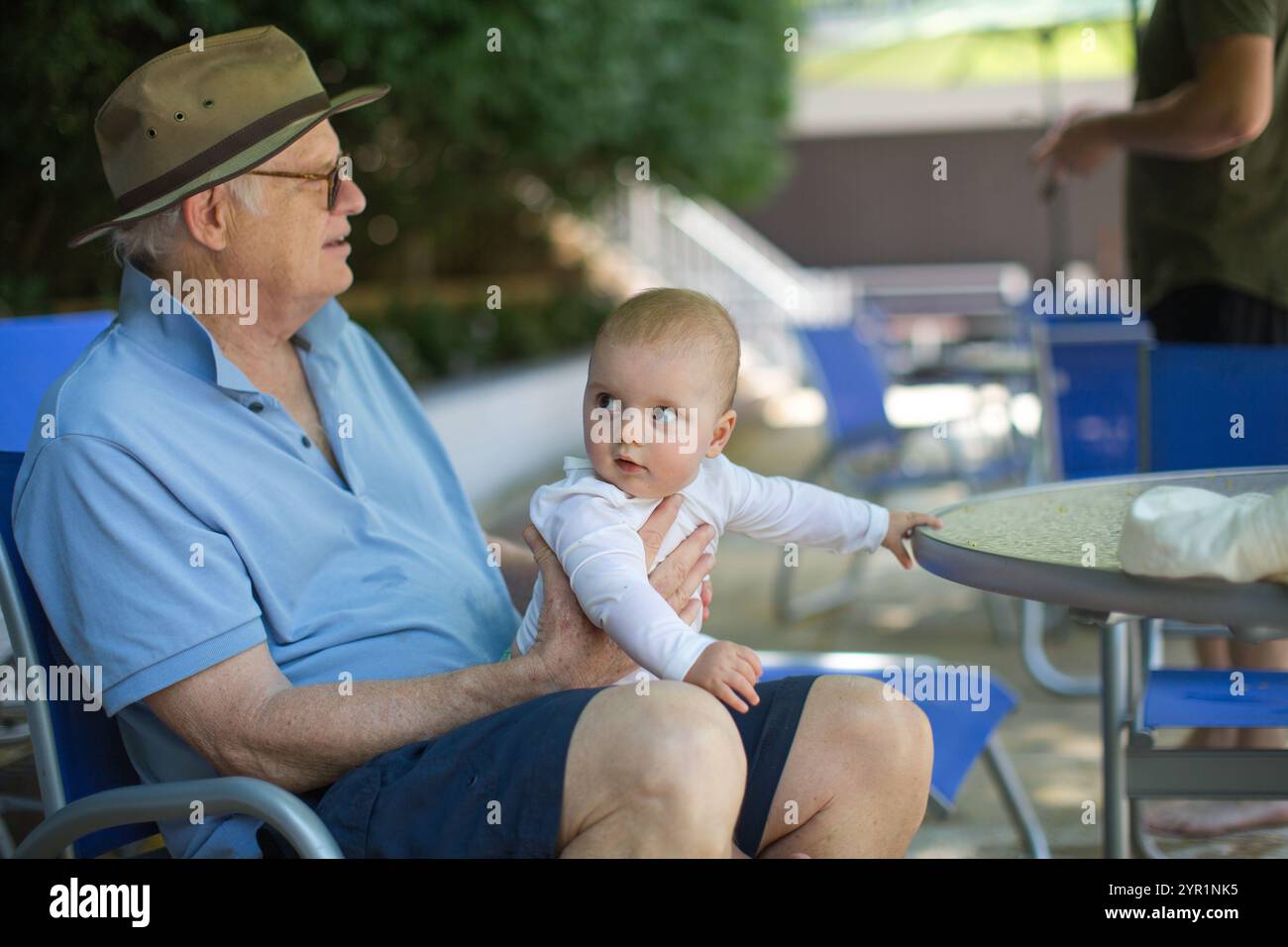 nonno seduto sulla terrazza della piscina con il nipote neonato in braccio Foto Stock