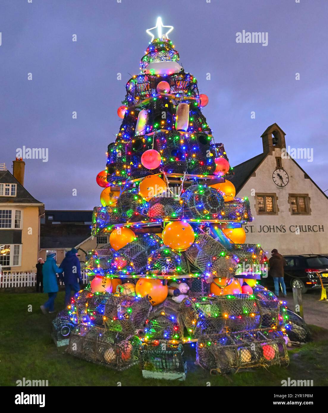 West Bay, Dorset, Regno Unito. 1 dicembre 2024. Le luci su un albero di Natale unico di quasi 24 metri, composto da vasi di aragosta, parafanghi e boe, sono state illuminate al crepuscolo sul verde di West Bay nel Dorset dal sindaco di Bridport Anne Rickard e dal Gwynedd Short di 100 anni, il più anziano residente. All'evento hanno partecipato una grande folla che è stata intrattenuta dal Bridport e dal Dorchester Rock Choir. 1 dicembre 2024. Foto: Graham Hunt Alamy Live News Foto Stock
