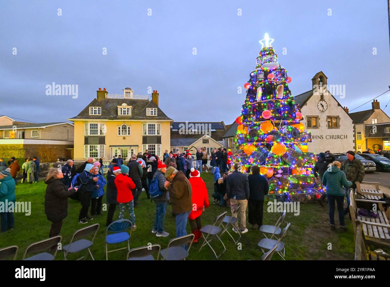 West Bay, Dorset, Regno Unito. 1 dicembre 2024. Le luci su un albero di Natale unico di quasi 24 metri, composto da vasi di aragosta, parafanghi e boe, sono state illuminate al crepuscolo sul verde di West Bay nel Dorset dal sindaco di Bridport Anne Rickard e dal Gwynedd Short di 100 anni, il più anziano residente. All'evento hanno partecipato una grande folla che è stata intrattenuta dal Bridport e dal Dorchester Rock Choir. La folla circonda l'albero per scattare foto. 1 dicembre 2024. Foto: Graham Hunt Alamy Live News Foto Stock