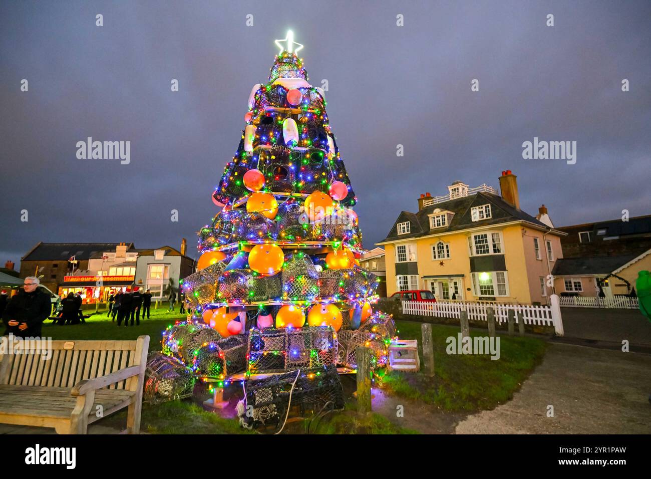 West Bay, Dorset, Regno Unito. 1 dicembre 2024. Le luci su un albero di Natale unico di quasi 24 metri, composto da vasi di aragosta, parafanghi e boe, sono state illuminate al crepuscolo sul verde di West Bay nel Dorset dal sindaco di Bridport Anne Rickard e dal Gwynedd Short di 100 anni, il più anziano residente. All'evento hanno partecipato una grande folla che è stata intrattenuta dal Bridport e dal Dorchester Rock Choir. 1 dicembre 2024. Foto: Graham Hunt Alamy Live News Foto Stock