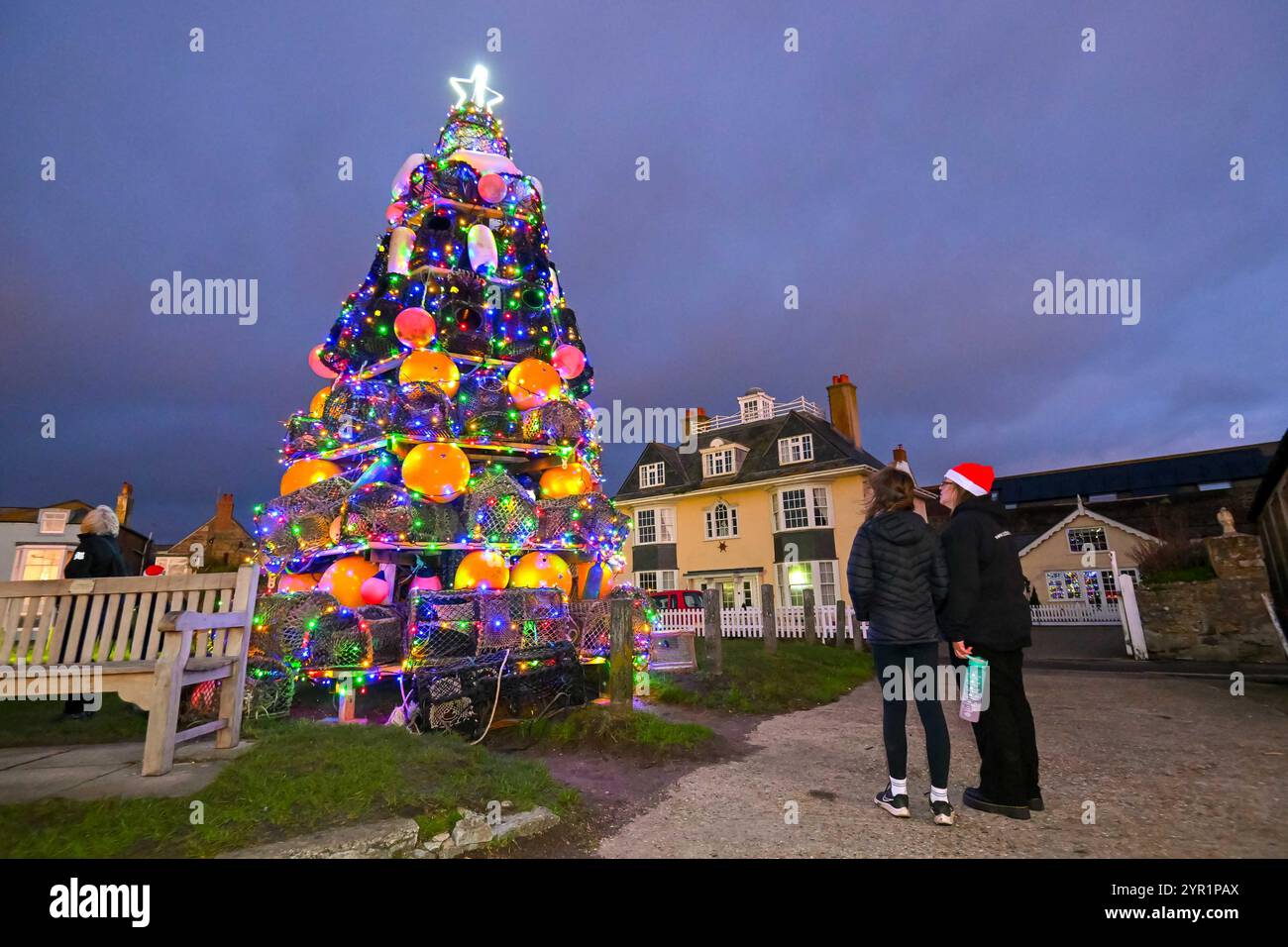 West Bay, Dorset, Regno Unito. 1 dicembre 2024. Le luci su un albero di Natale unico di quasi 24 metri, composto da vasi di aragosta, parafanghi e boe, sono state illuminate al crepuscolo sul verde di West Bay nel Dorset dal sindaco di Bridport Anne Rickard e dal Gwynedd Short di 100 anni, il più anziano residente. All'evento hanno partecipato una grande folla che è stata intrattenuta dal Bridport e dal Dorchester Rock Choir. 1 dicembre 2024. Foto: Graham Hunt Alamy Live News Foto Stock