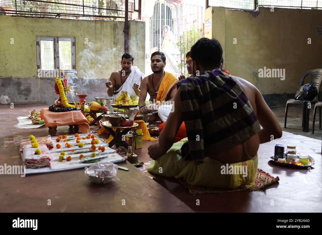 Un gruppo di quattro uomini indù seduti a croce zampe in un tempio di Kolkata in India pregando con incenso bruciante e offerte floreali su un alter Foto Stock