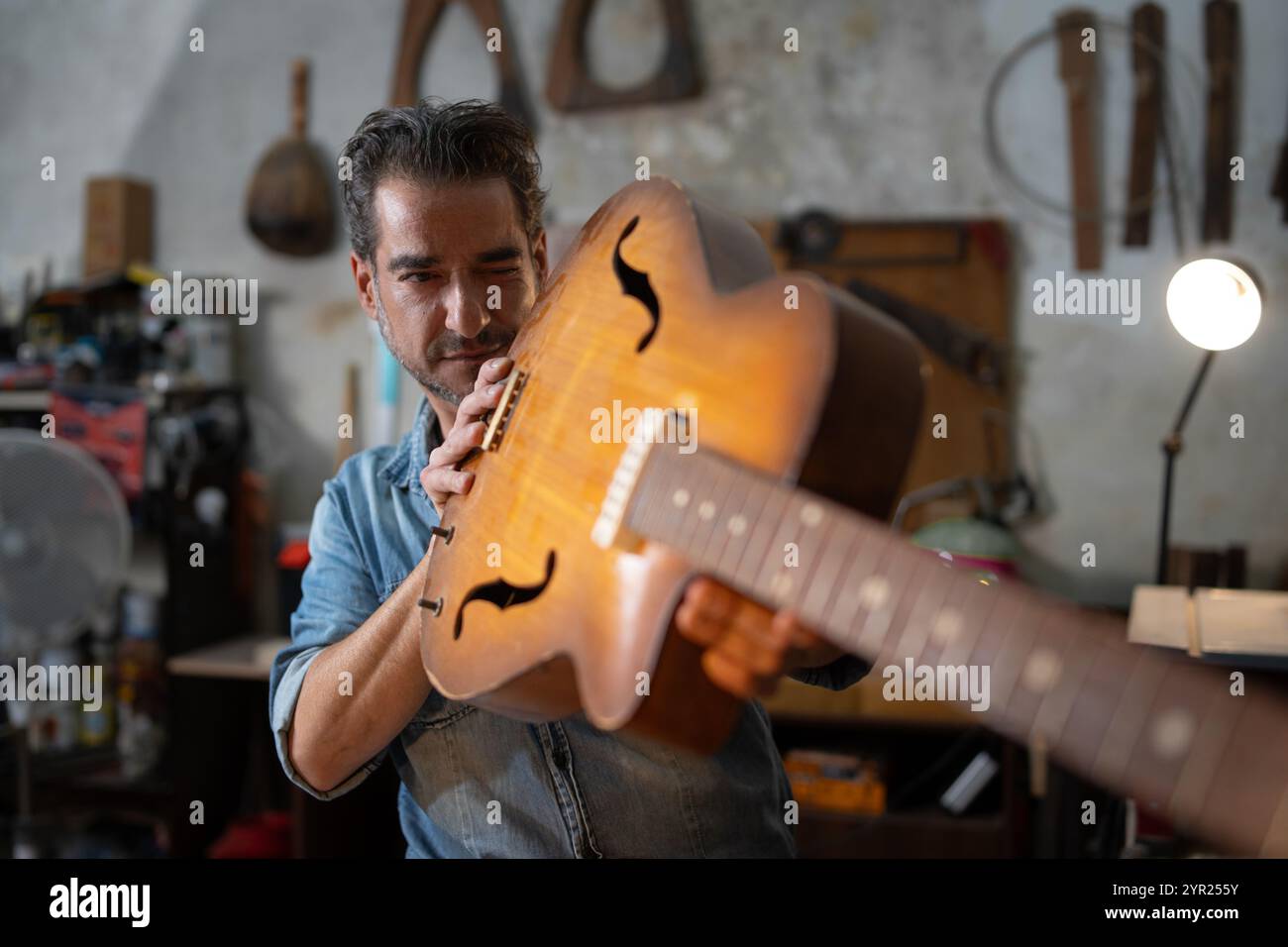 Produttore di chitarre professionista che ispeziona i dettagli della chitarra acustica in un'officina tradizionale. Artigiano ispanico che esamina gli strumenti d'epoca mostrando esperti Foto Stock