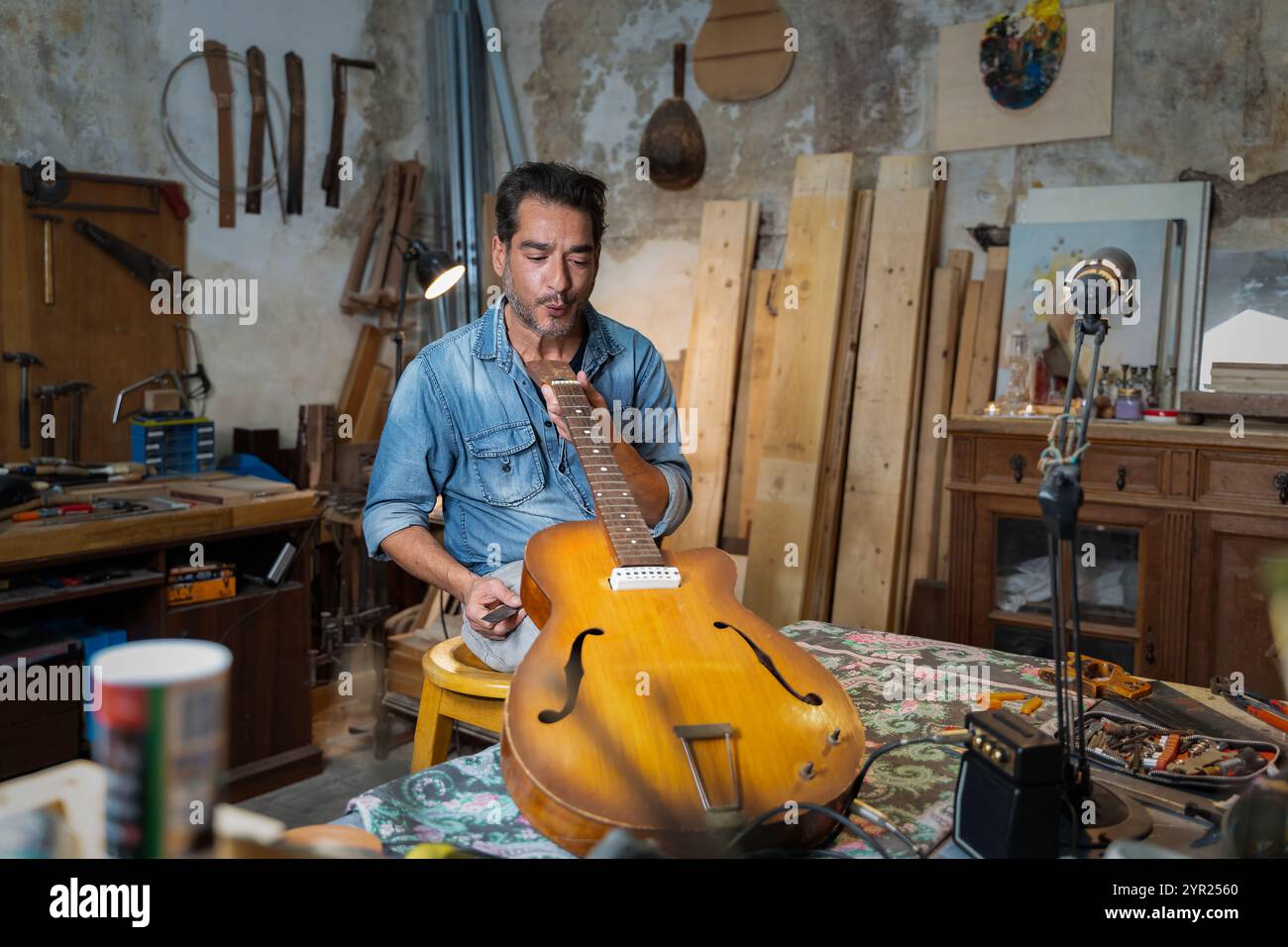 Liutaio esperto che lavora alla chitarra acustica in un autentico laboratorio. Artigiano esperto che ripara strumenti musicali d'epoca con strumenti tradizionali Foto Stock