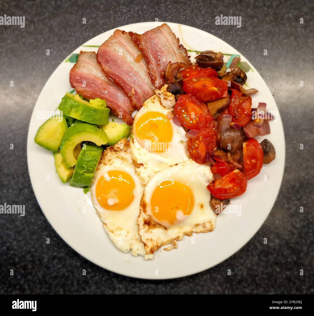 Piatto da pranzo decorato con ingredienti a basso contenuto di carboidrati come pancetta fritta con uova fritte, accanto ad essa un'insalata di funghi fritti, pomodori e cipolla Foto Stock