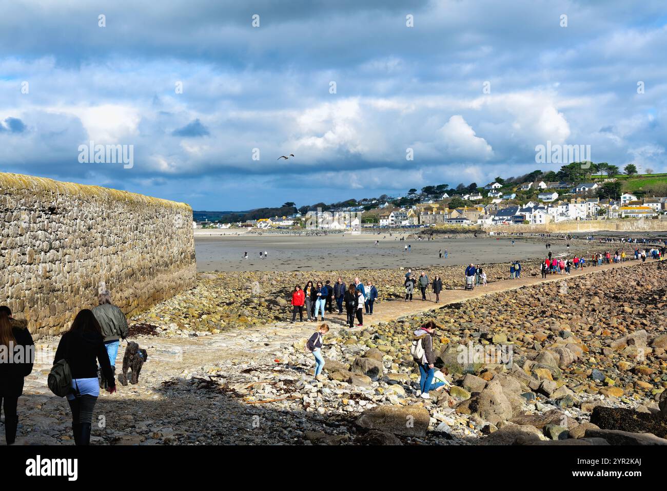 Persone che camminano sulla strada sopraelevata pubblica tra il monte St Michaels e il villaggio di Marazion, con la bassa marea, in Cornovaglia, Inghilterra, Regno Unito Foto Stock