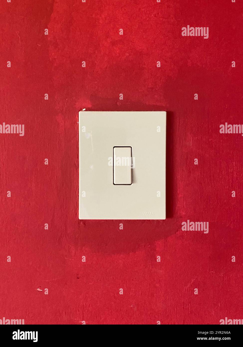 Un interruttore luminoso minimalista posizionato contro una parete rossa. Foto Stock