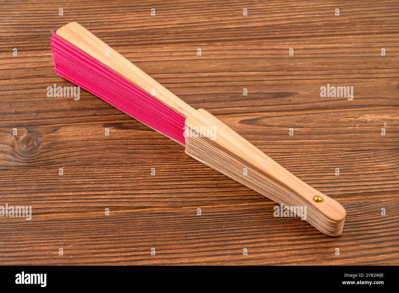 Questo ventilatore a mano, realizzato in modo splendido, è piegato e appoggiato su una superficie rustica in legno Foto Stock