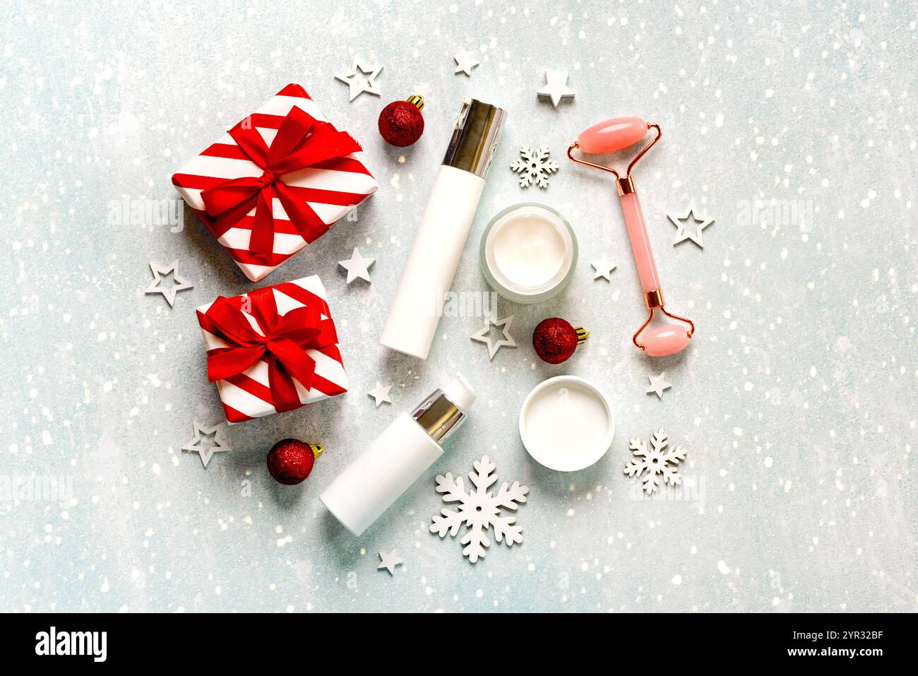 Vista dall'alto dei prodotti per la cura della pelle, rullo massaggiatore in giada, palline di natale rosse e scatole regalo di natale sullo sfondo natalizio. Concetto di bellezza in cristo Foto Stock