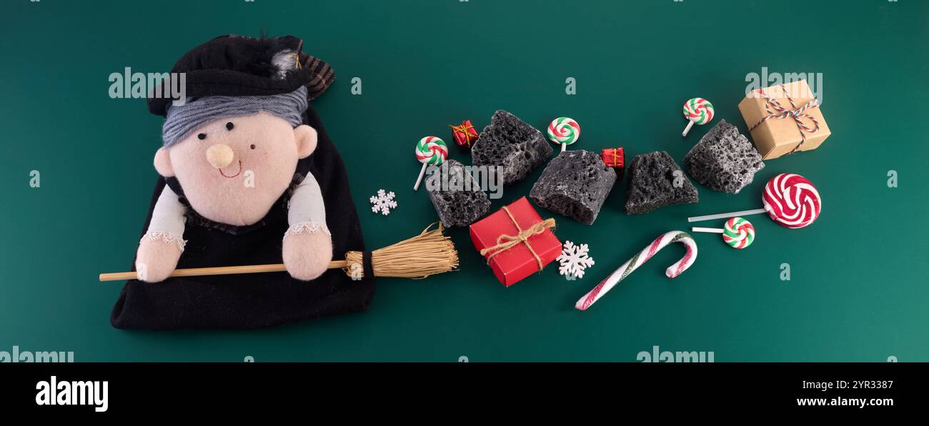 La Befana con carbone dolce e caramelle su sfondo verde. Tradizione italiana del giorno dell'Epifania Foto Stock