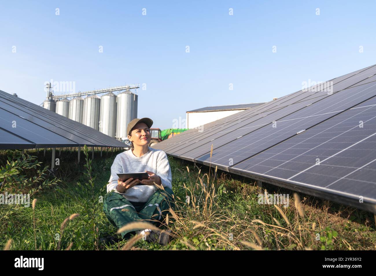 Agricoltore donna con tablet digitale in una moderna azienda agricola che utilizza pannelli solari. Silos agricoli sullo sfondo. Foto Stock