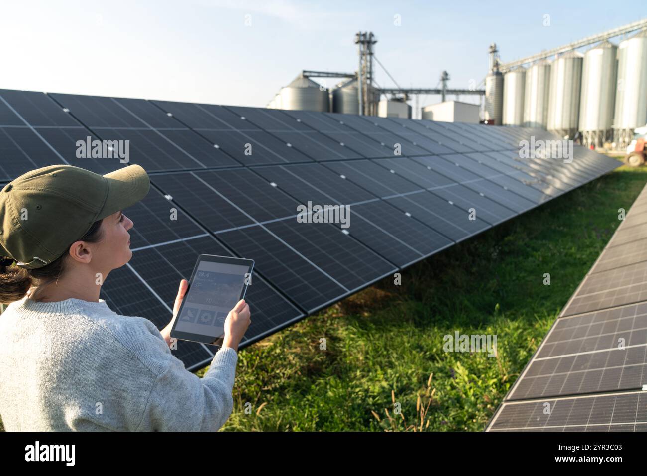 Agricoltore donna con tablet digitale in una moderna azienda agricola che utilizza pannelli solari. Silos agricoli sullo sfondo. Foto Stock