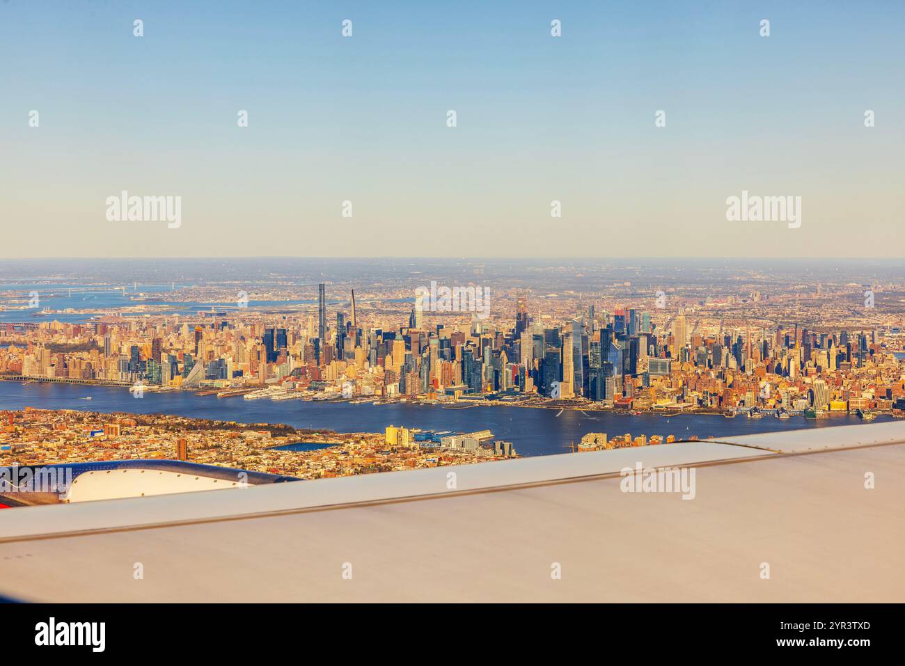 Vista aerea dello skyline di Manhattan con il fiume Hudson e gli iconici grattacieli durante l'ora d'oro dalla finestra dell'aereo in volo. STATI UNITI. Foto Stock
