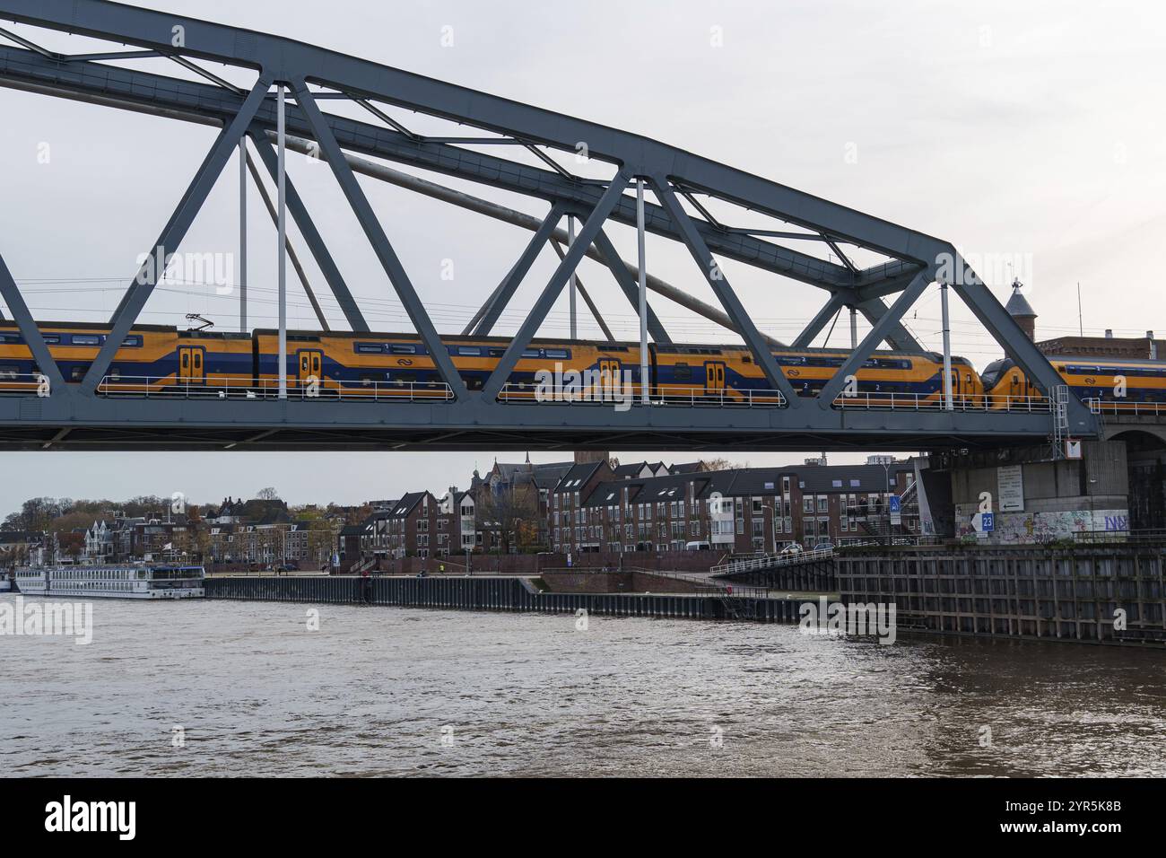 Moderno treno che attraversa un ponte ferroviario industriale su un fiume, architettura urbana sullo sfondo, nijmegen, waal, gheldria, paesi bassi Foto Stock