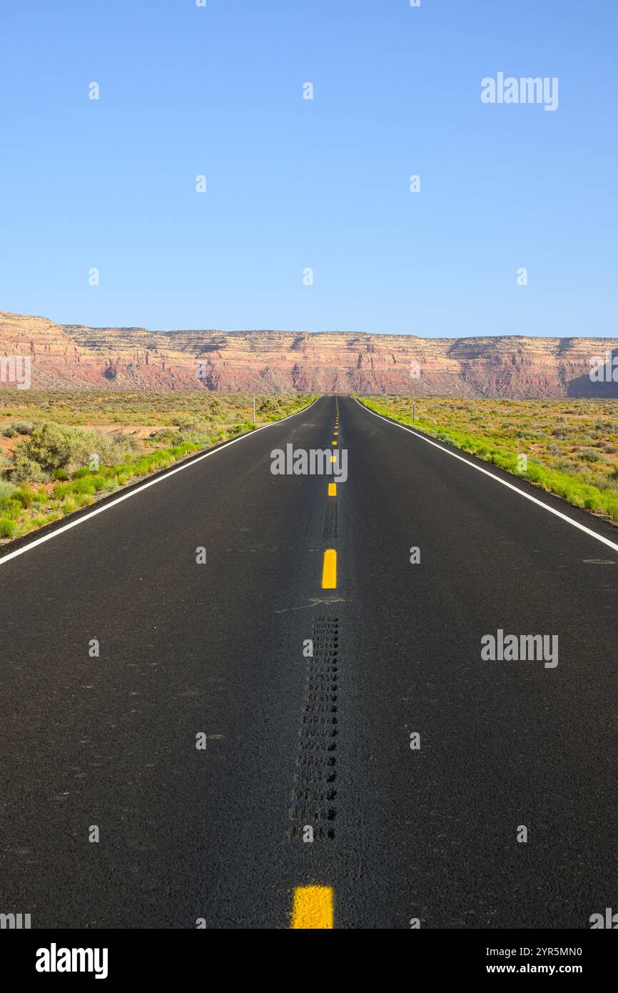 Autostrada desertica asfaltata nera che si estende fino a lontane colline rosse Foto Stock