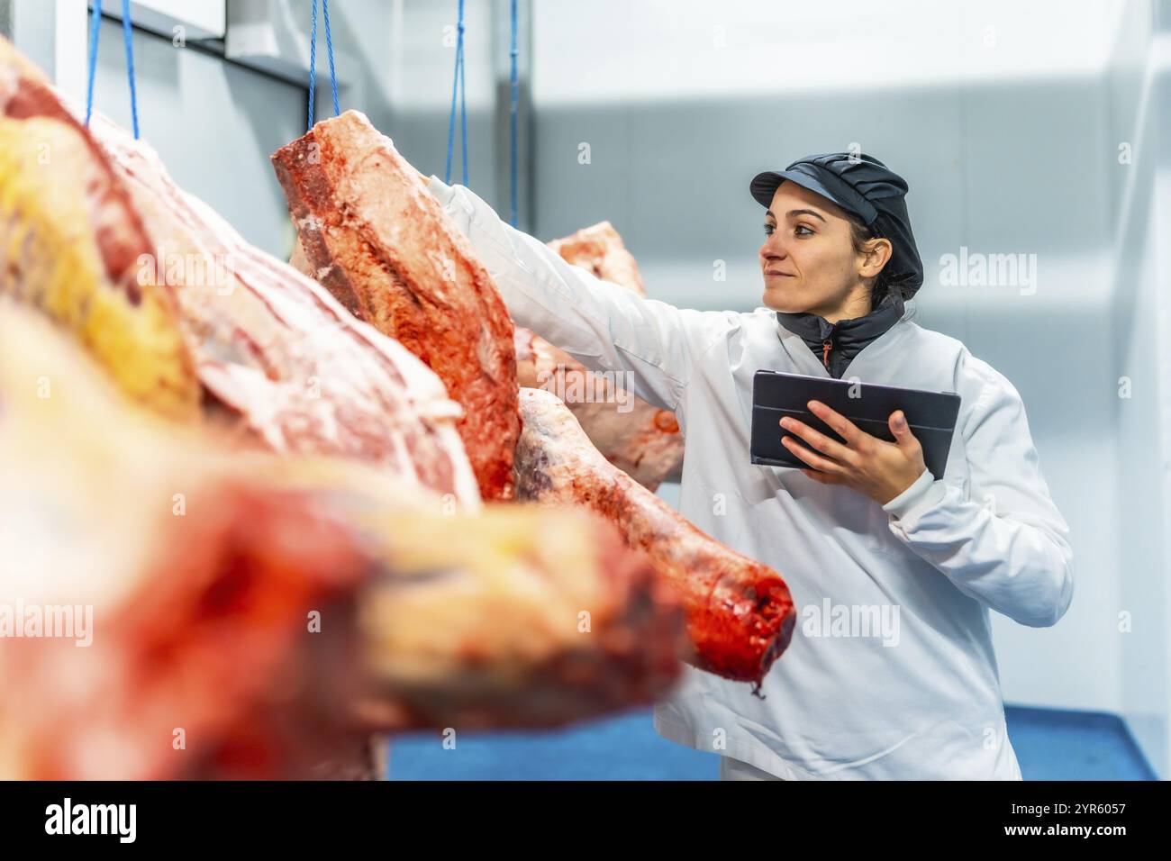 Macelleria femminile che utilizza un tablet digitale per analizzare i prodotti in un magazzino per la carne fredda Foto Stock