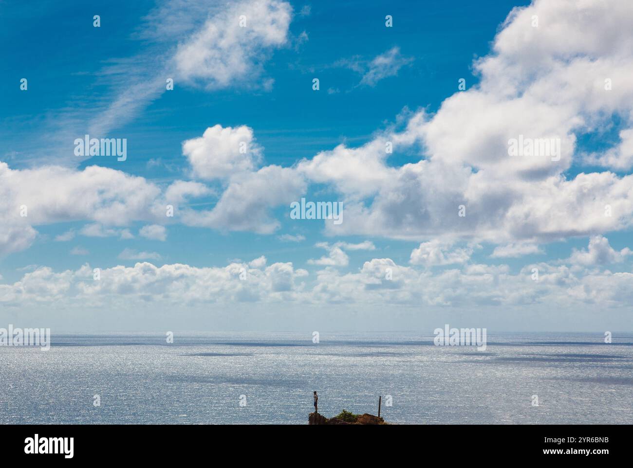 Vista mozzafiato del vasto oceano scintillante sotto un cielo dinamico pieno di soffici nuvole bianche a nazare, in portogallo. Uomo in cima a una roccia. Foto Stock