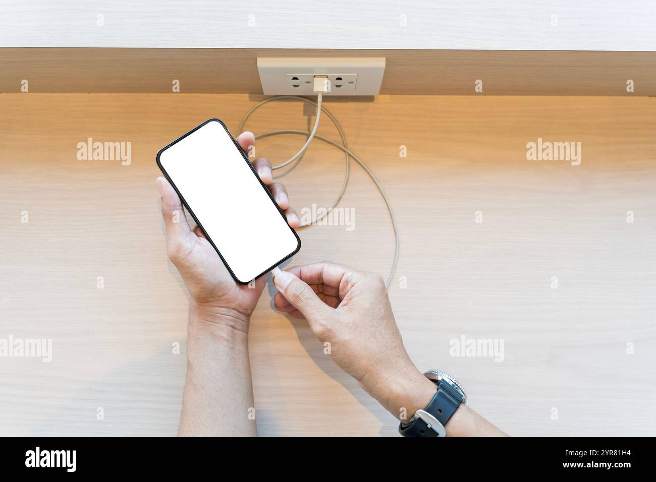 Man: Collega il cavo micro usb allo smartphone con schermo bianco vuoto per ricaricare la batteria del telefono sul tavolo. Tracciato di ritaglio. Foto Stock