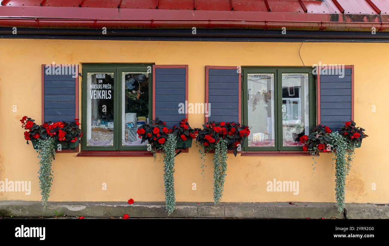 Talsi, Lettonia - 1° settembre 2024: Una casa con persiane colorate che presenta vivaci fiori rossi sotto le sue finestre. Foto Stock