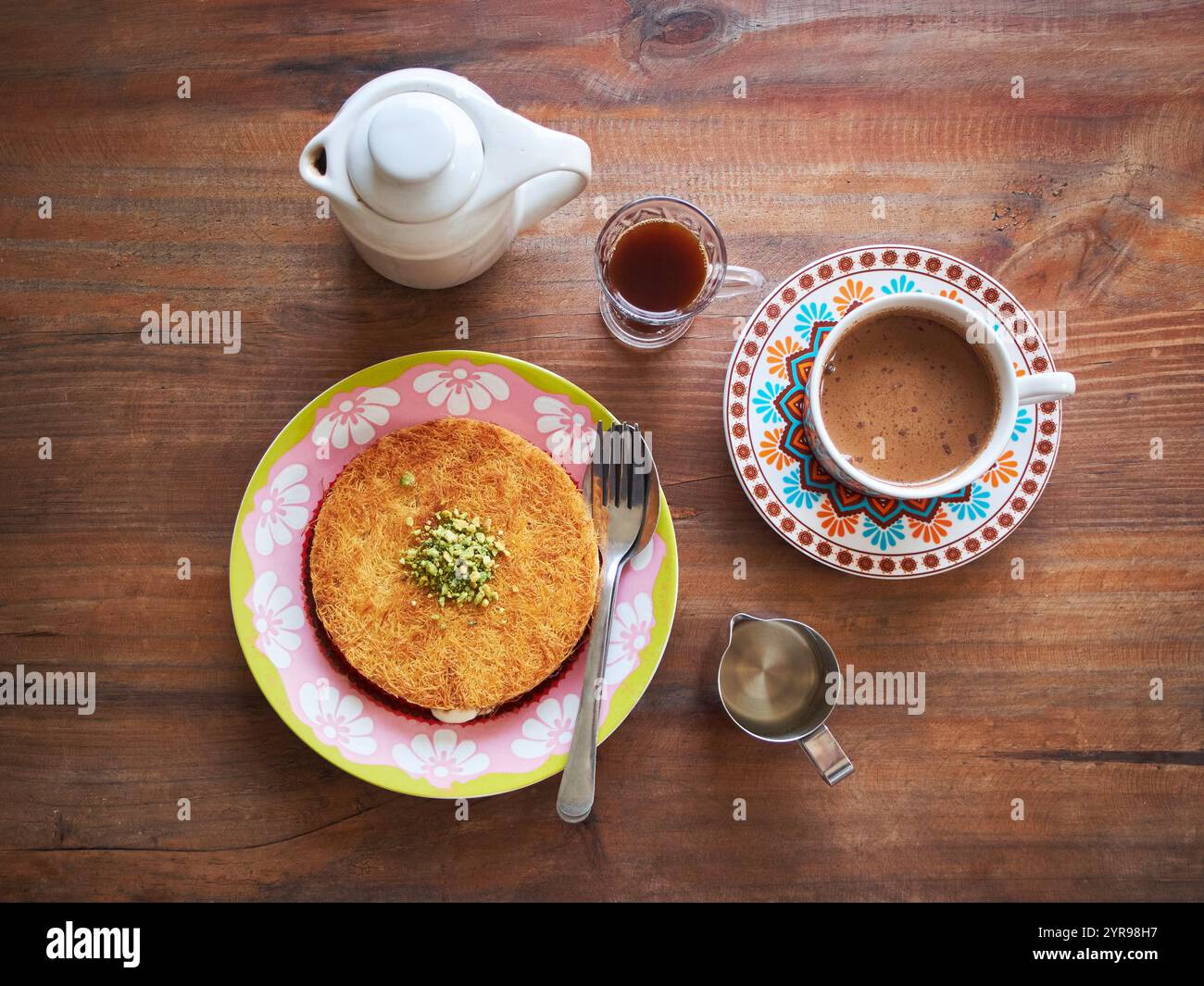 Kunafa o Kunefe è un dolce tradizionale mediorientale. Servito con caffè turco e caffè speziato su un tavolo di legno Foto Stock