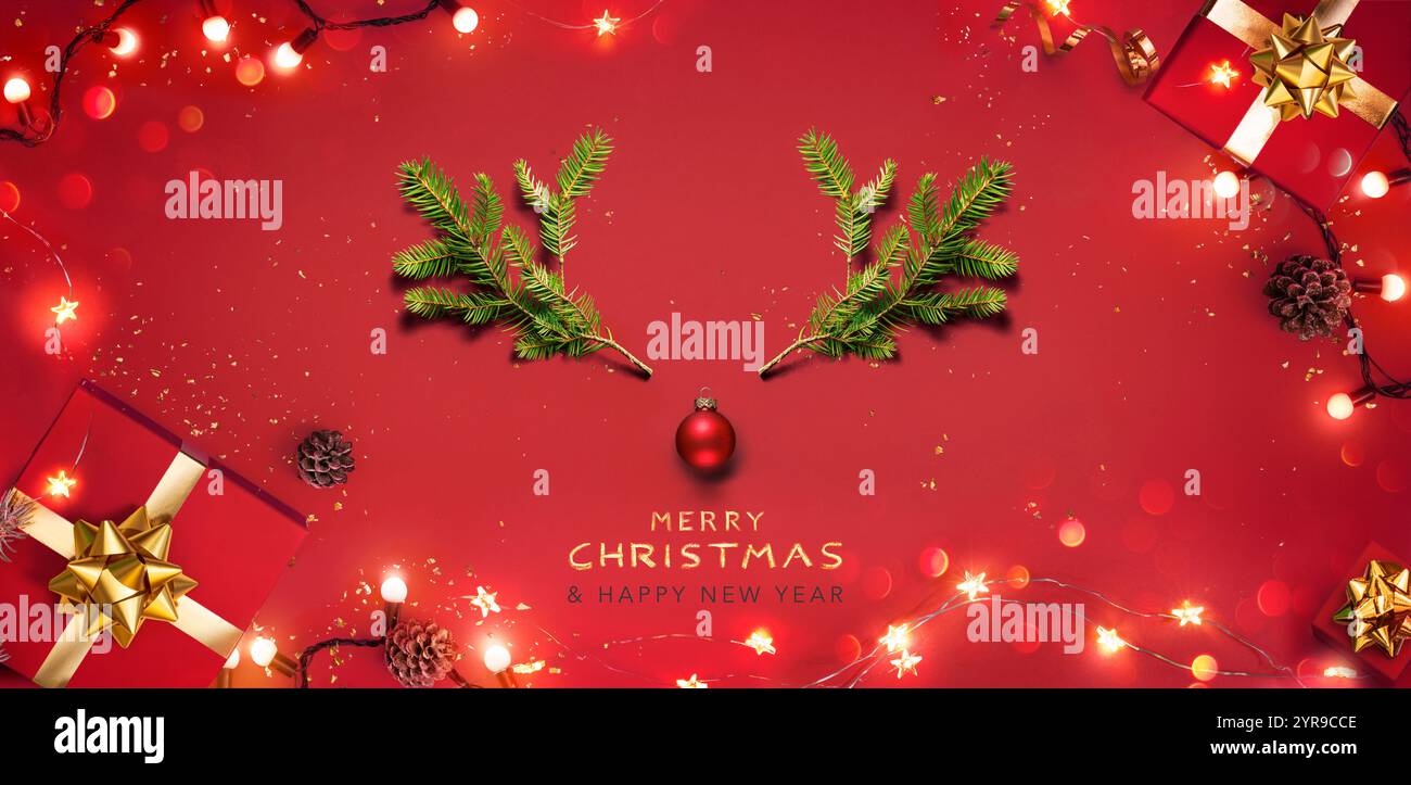Sfondo rosso di Natale - cervo con rami di Fir verde elementi e confezioni regalo - Vista a piano superiore natalizio con decorazioni luccicanti della ghirlanda Foto Stock