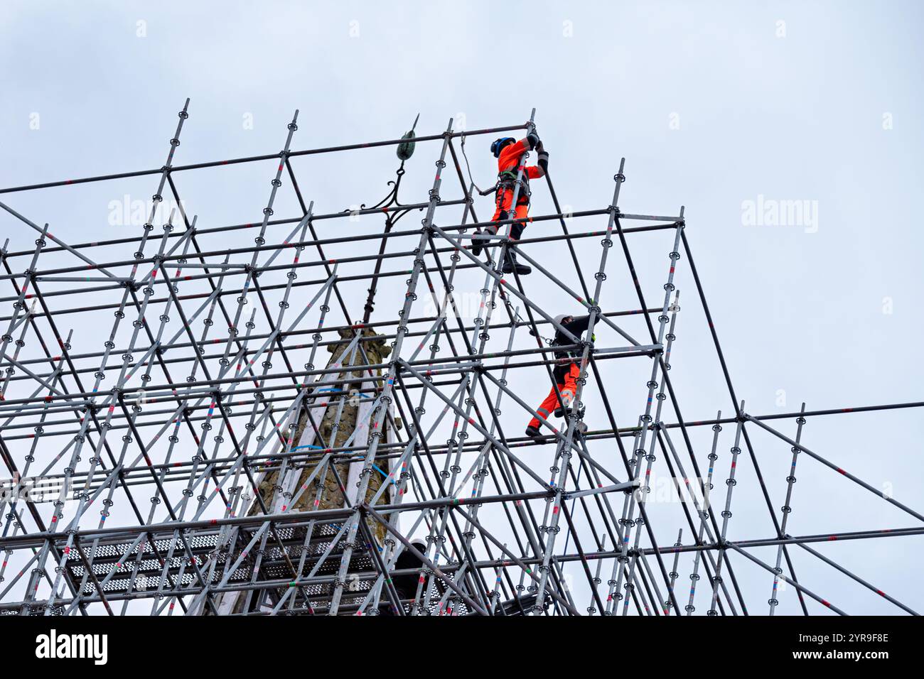 Due lavoratori qualificati con attrezzature di sicurezza che installano impalcature in cima alla chiesa di San Tommaso di Canterbury per ripristinare la guglia danneggiata. Foto Stock