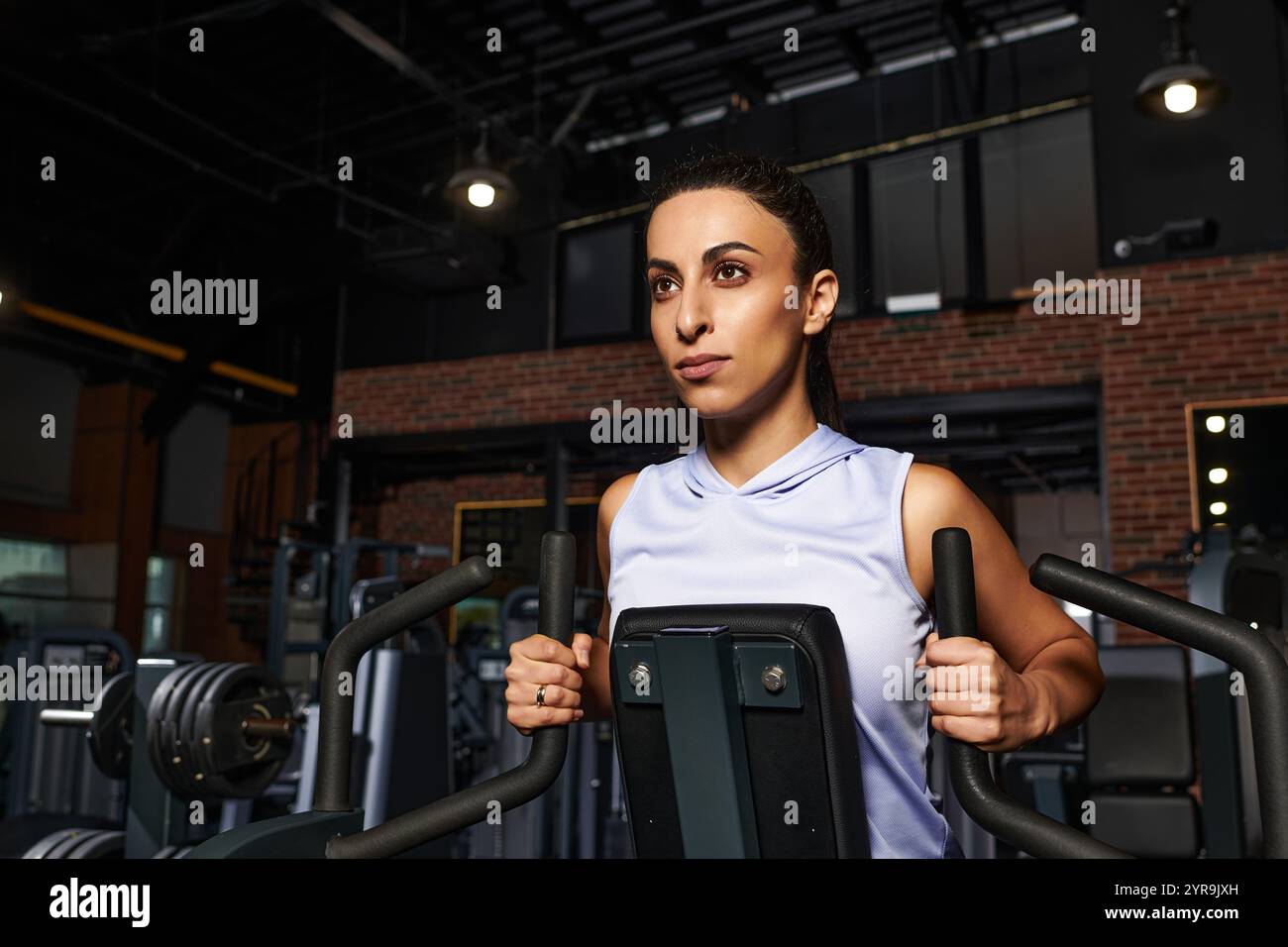 Una donna dedicata lavora sulla forza della parte superiore del corpo utilizzando le attrezzature da palestra in un ambiente energico. Foto Stock