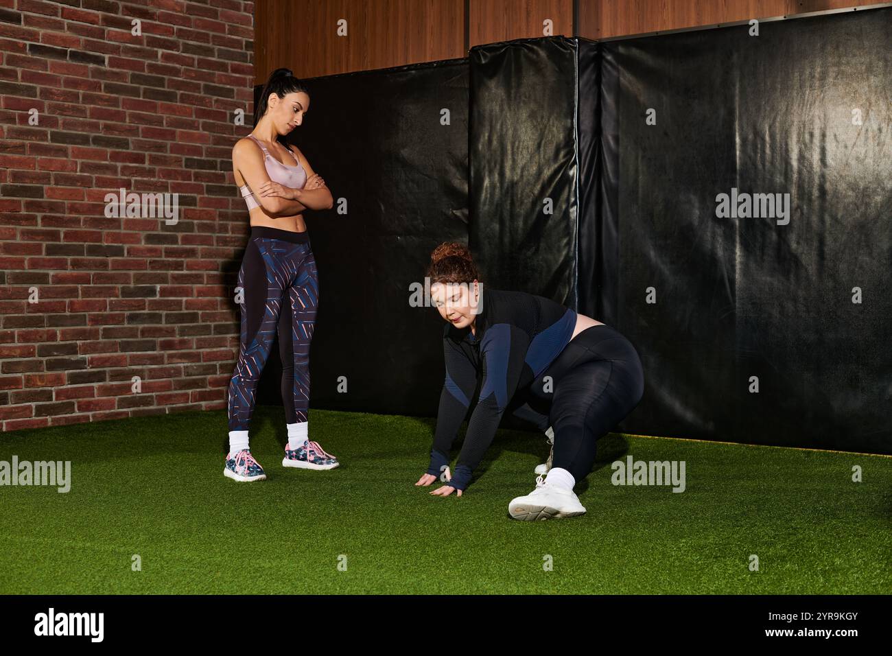 Due donne dimostrano diverse tecniche di allenamento in una palestra dall'atmosfera vivace. Foto Stock