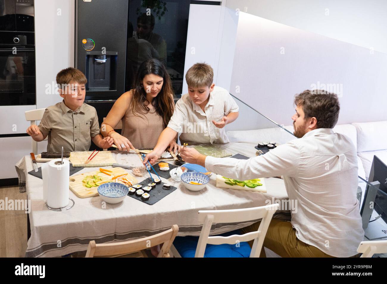 Famiglia caucasica che prepara sushi insieme nella loro cucina moderna, godendo del tempo di qualità Foto Stock