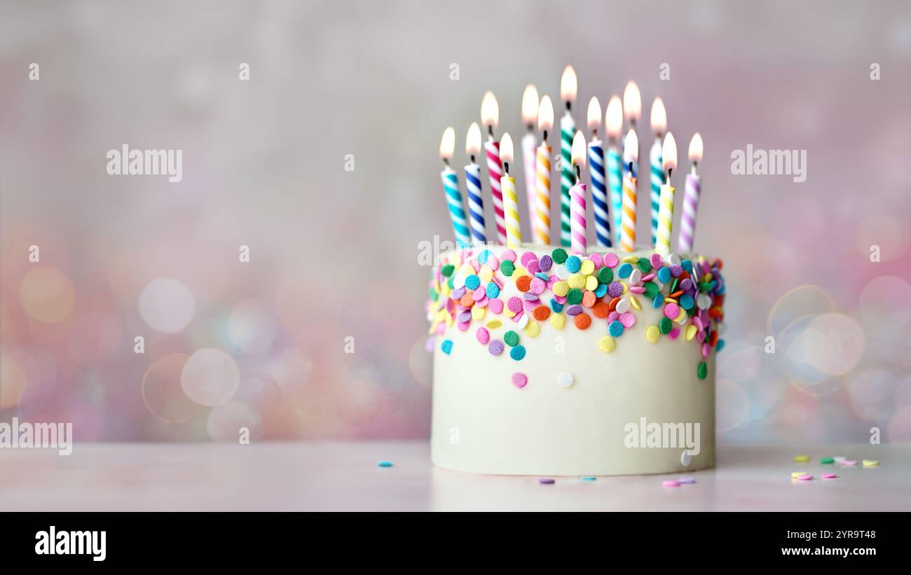 Colorata torta di compleanno con spruzzette di zucchero e candele di compleanno colorate sullo sfondo di luci fiabesche sfocate Foto Stock