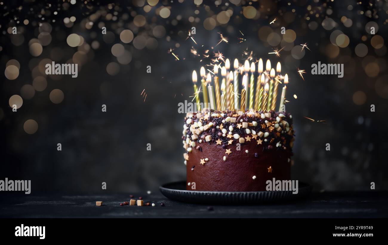 Torta al cioccolato decorata con molte candele d'oro per il compleanno e scintillanti Foto Stock