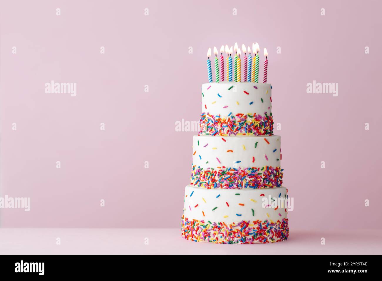 Torta di compleanno a più piani con colorate cospargette di zucchero e dodici candele di compleanno Foto Stock