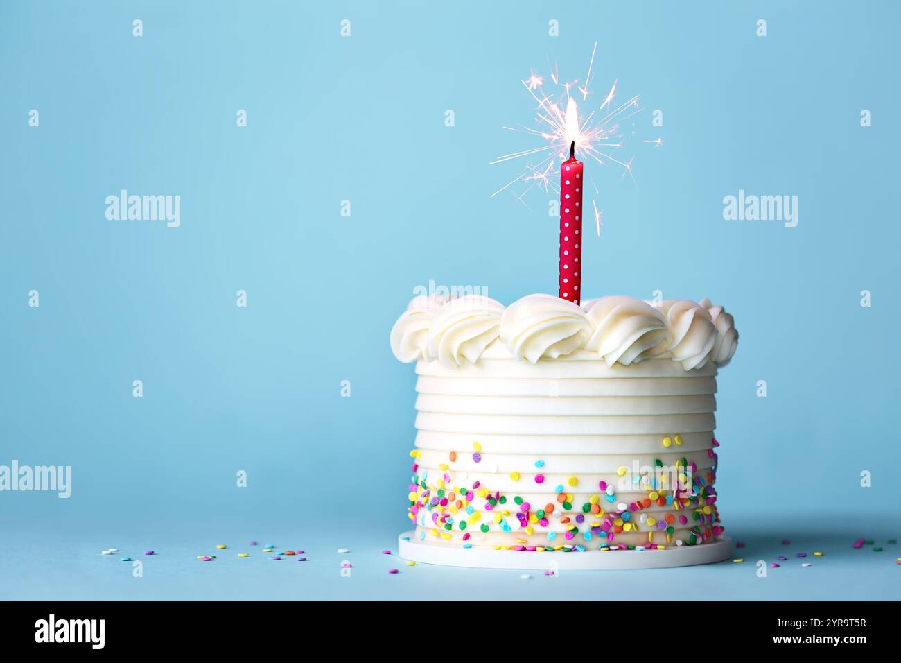 Torta di compleanno con spruzzette colorate e una candela di compleanno rossa su sfondo blu Foto Stock