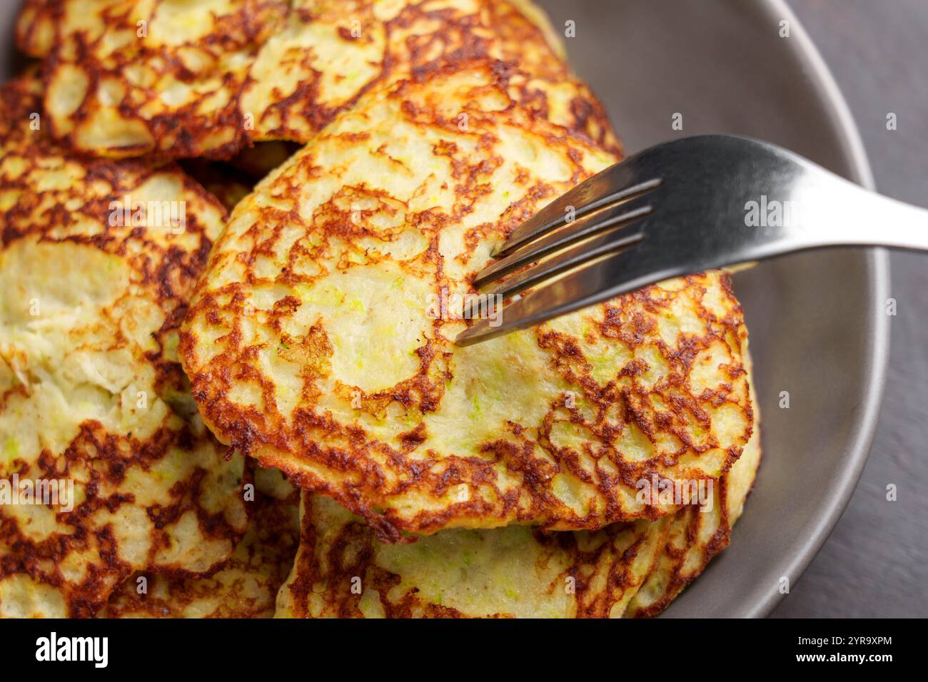 Frittelle cotte al momento preparate con zucchine grattugiate, latte di mandorle, uova e psicllium. Una forchetta argentata poggia sulla superficie dorata croccante. Perfetto per la guarigione Foto Stock