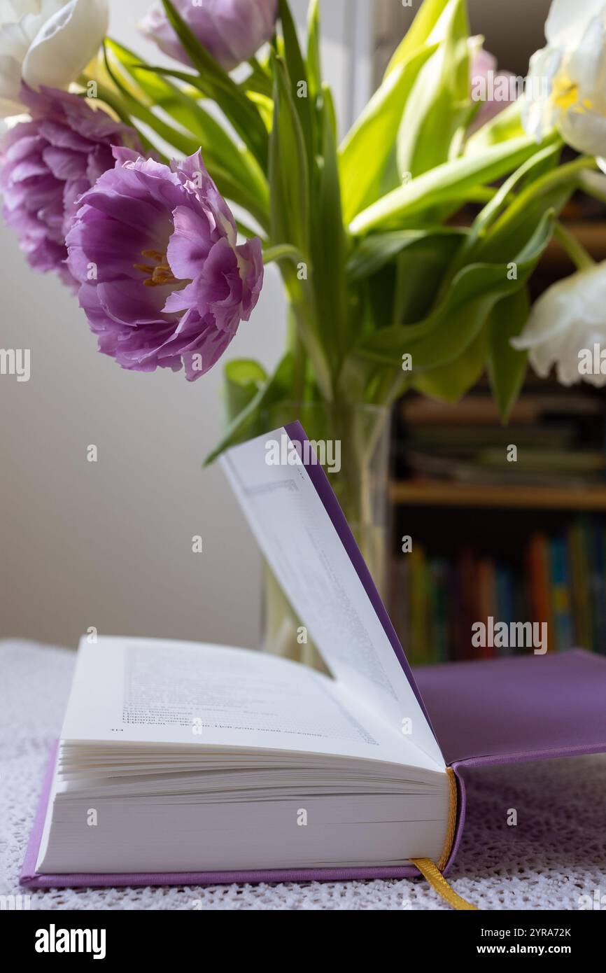 sul tavolo c'è un libro con poesie e un vaso con fiori di tulipani nelle vicinanze. Mattinata accogliente, piacevole solitudine. Semplice gioia umana. Book Day, buona lettura Foto Stock
