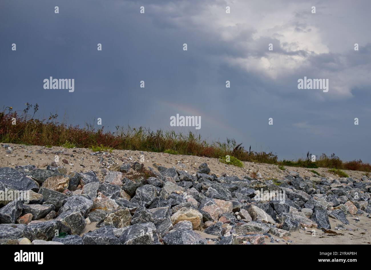 Vista dalla costa baltica verso la terra su una striscia costiera di sabbia e rocce e un arcobaleno a Schönhagen, Mar Baltico, Baia di Kiel, Germania Foto Stock