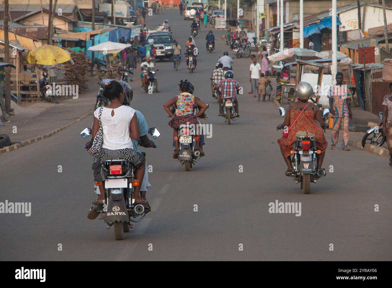 La trafficata Urban Street in Togo con motociclette, pedoni e negozi locali che raffigurano la vita quotidiana africana Foto Stock
