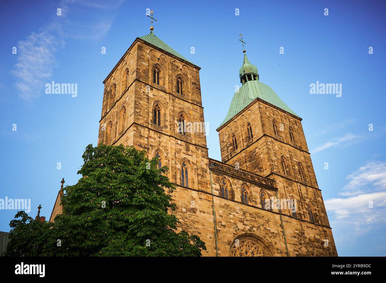 Una splendida vista di una storica chiesa in pietra con due alte torri, caratterizzata da tetti di rame verdi e intricati dettagli architettonici su un blu chiaro Foto Stock