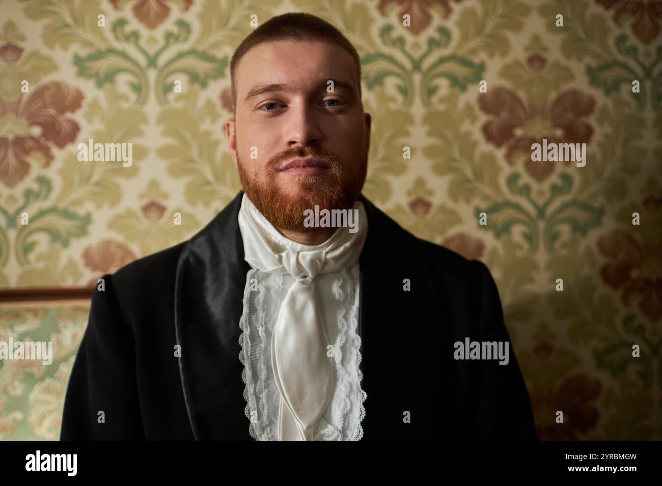 Ritratto della vista frontale di un giovane gentiluomo barbuto in costume classico che guarda la fotocamera con sfondo ornato, spazio copia Foto Stock