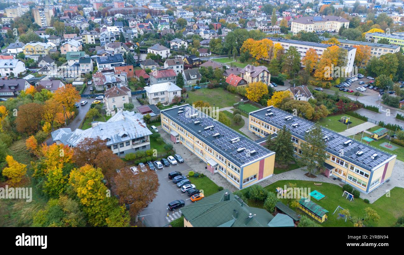 Vista aerea di un quartiere periferico con edifici residenziali, alberi e un complesso scolastico. L'area è circondata da vegetazione e vegetazione autunnale, Foto Stock