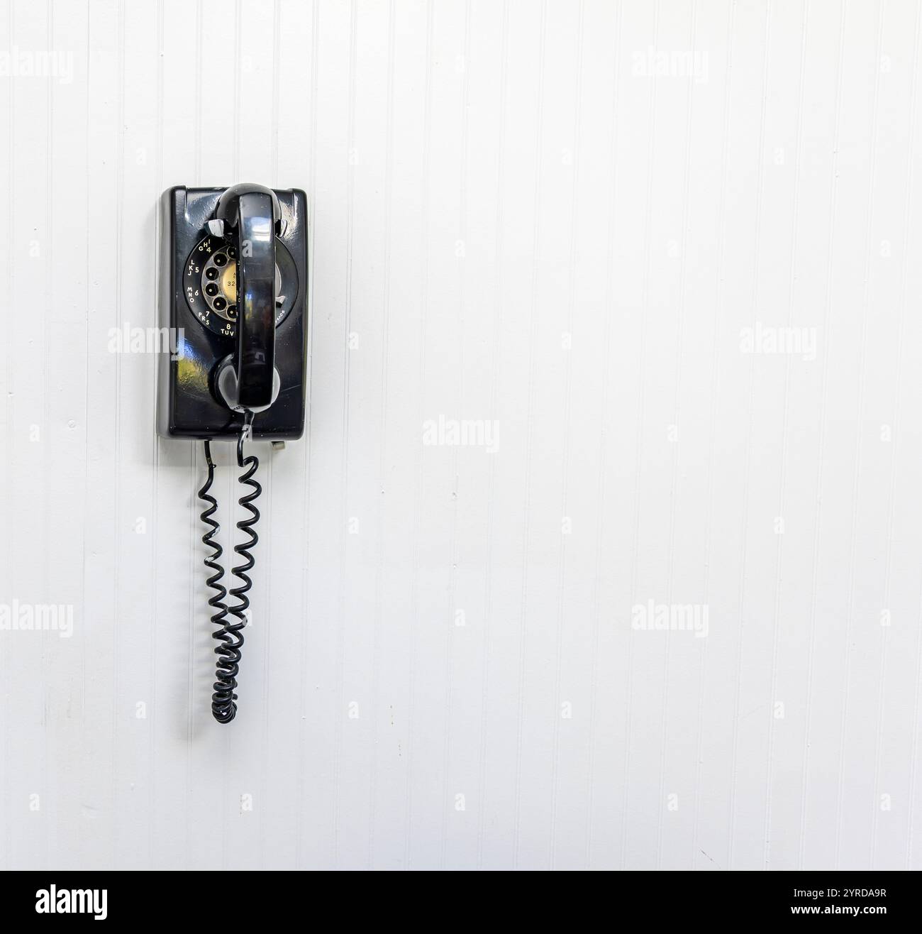 vecchio telefono rotante nero su una parete interna bianca Foto Stock