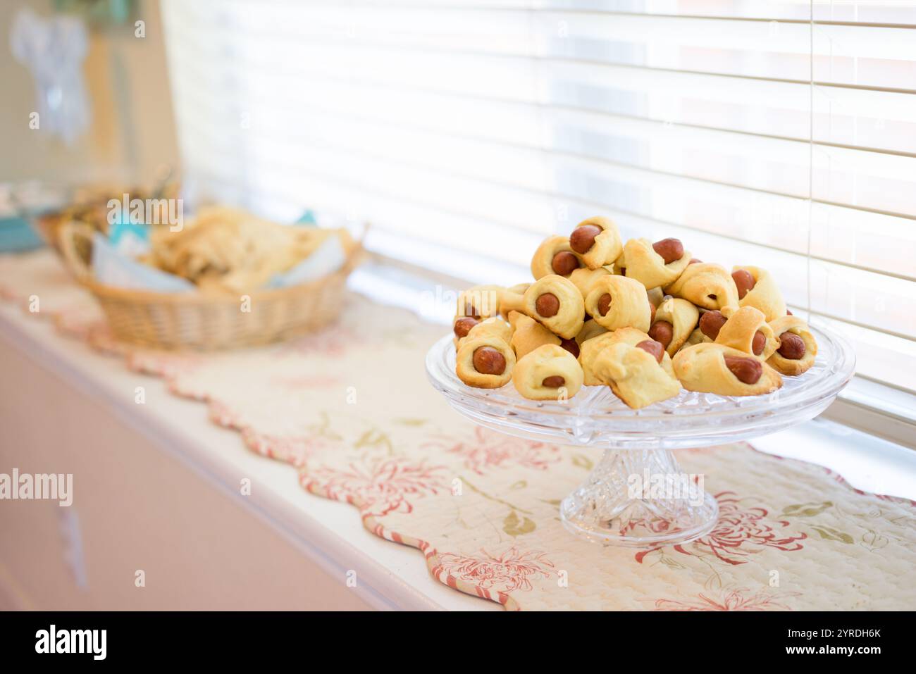 Mini Hot Dogs avvolti nella pasticceria su un piatto di portata in vetro vicino alla finestra Foto Stock