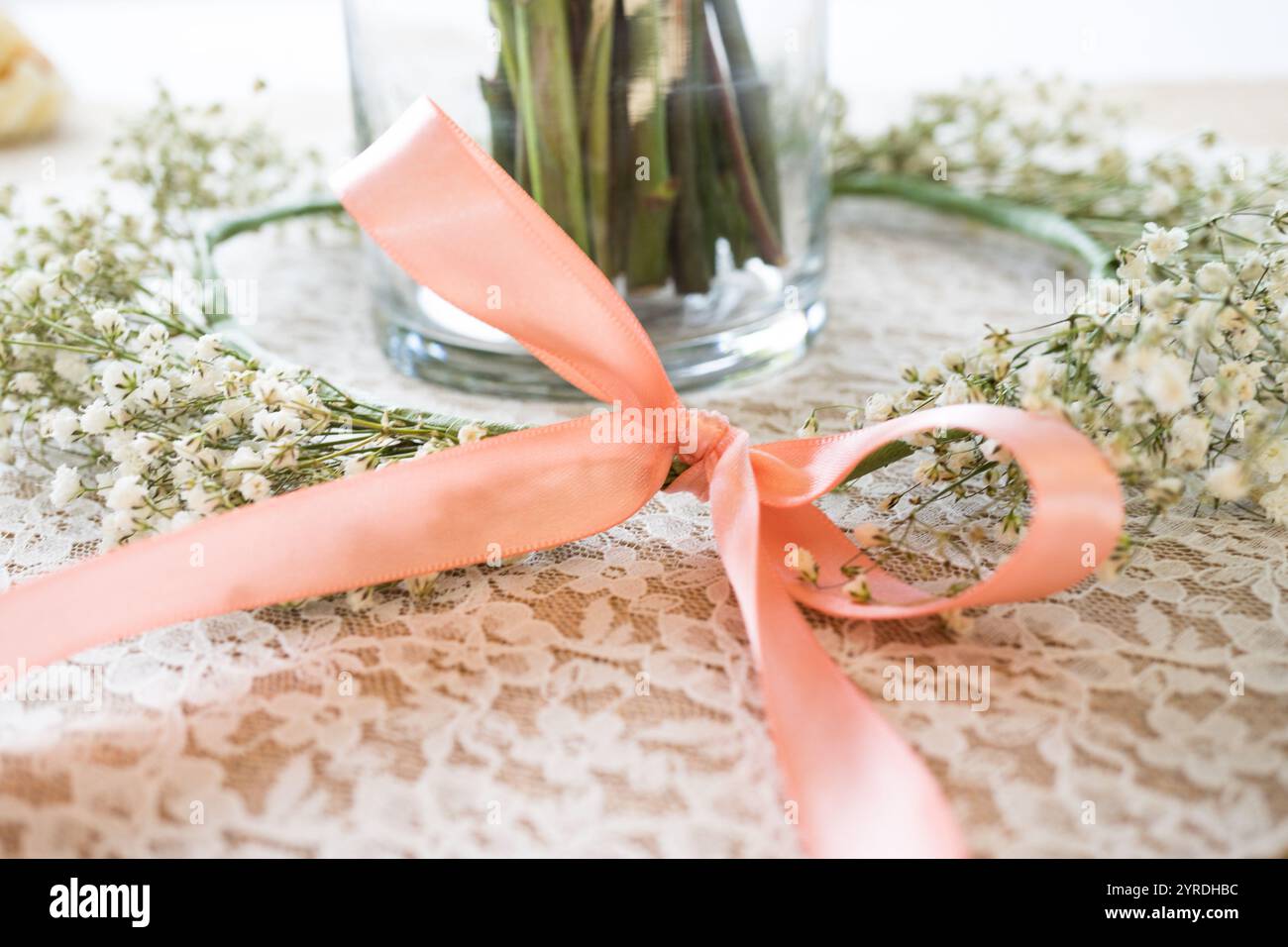 Delicata disposizione floreale con nastro di pesca e tovaglia in pizzo per il bambino Foto Stock