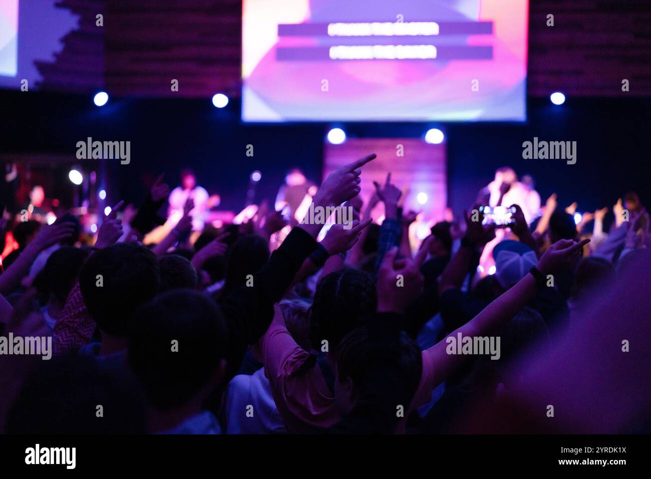 I concerti dei giovani adorano la folla in un evento musicale con le mani alzate e un'atmosfera entusiasta Foto Stock