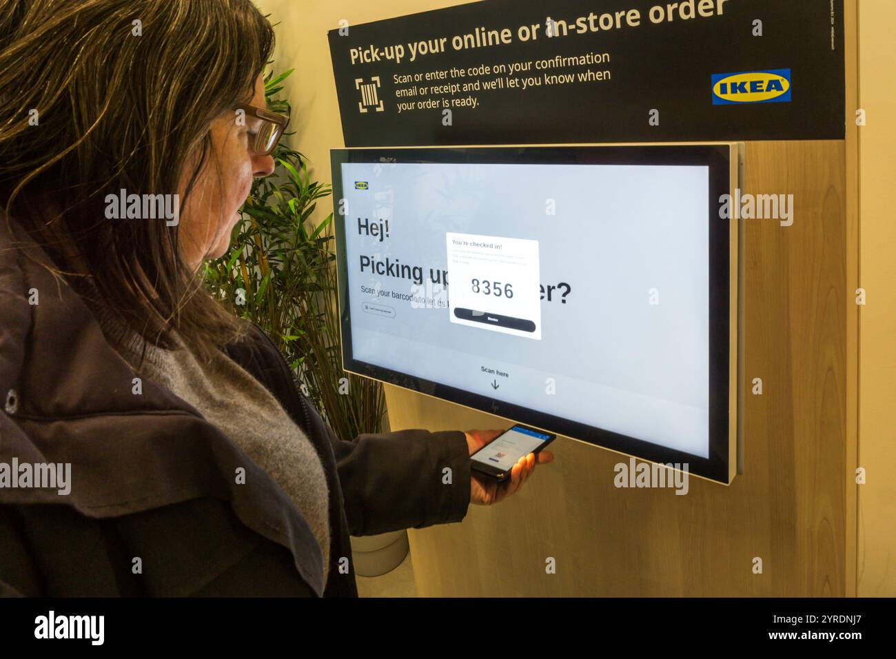 Donna che consente a un terminale di un negozio IKEA di leggere un codice a barre sul suo cellulare per ritirare un ordine online. Foto Stock